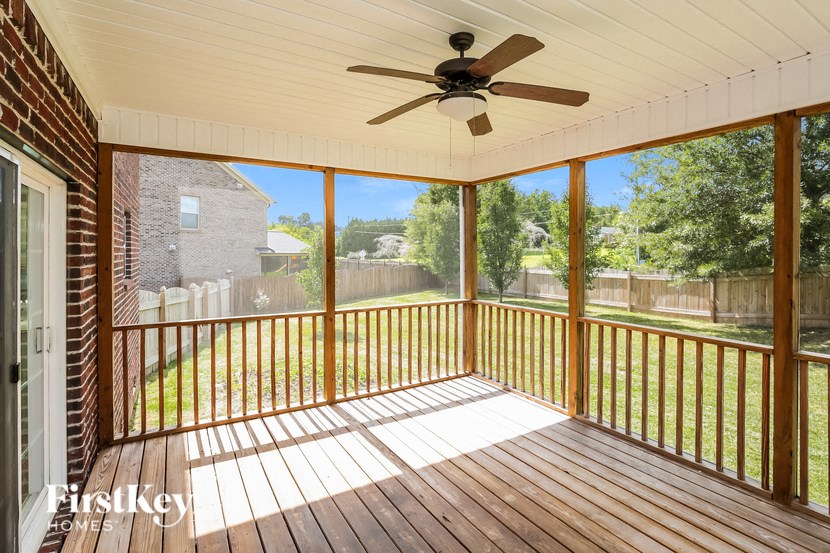 A wooden deck with a ceiling fan and a view of a backyard.