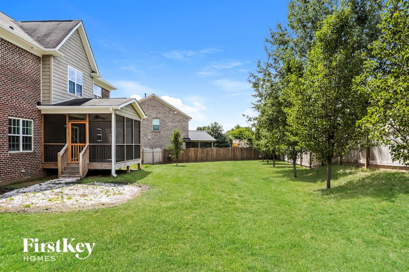 A house with a large lawn and a tree in front of a fence.