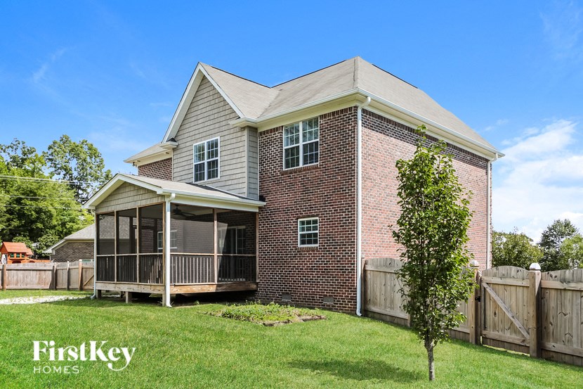A brick house with a porch and a tree in front.