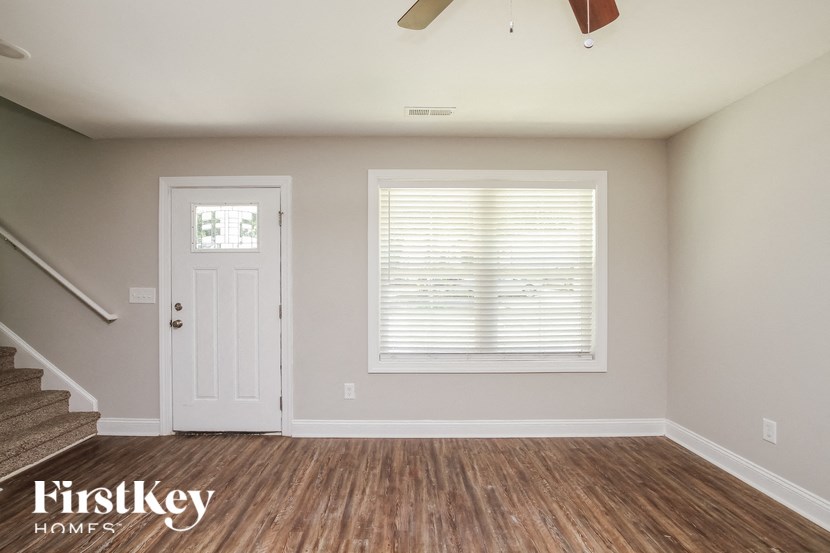 A room with a wooden floor, a staircase, a window with blinds, and a ceiling fan.