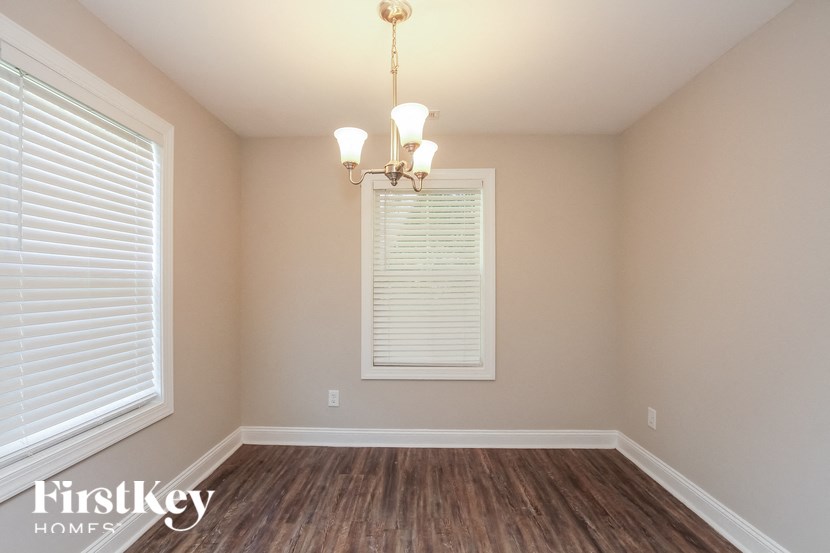 A room with a chandelier, a window with blinds, and wooden flooring.