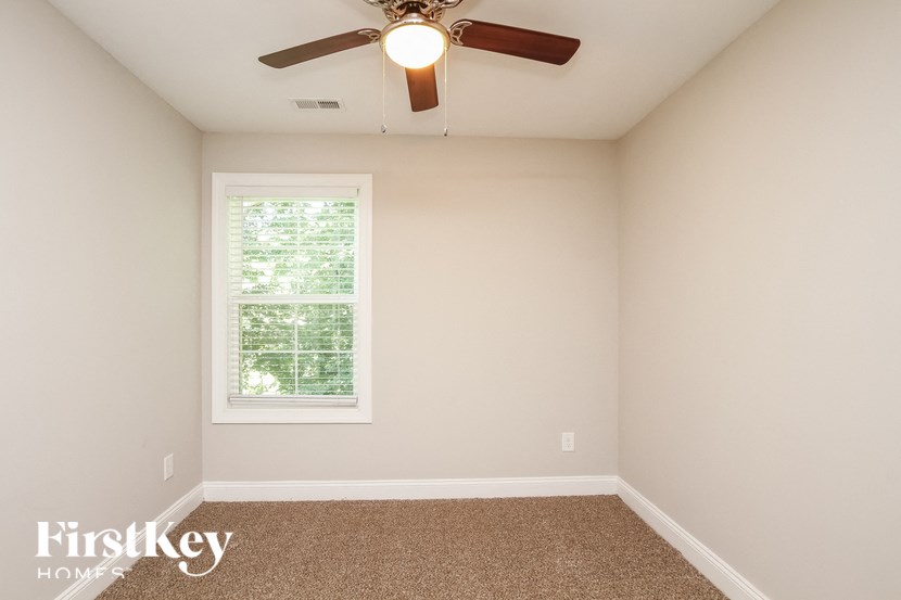 A room with a carpeted floor, a ceiling fan, and a window with blinds.