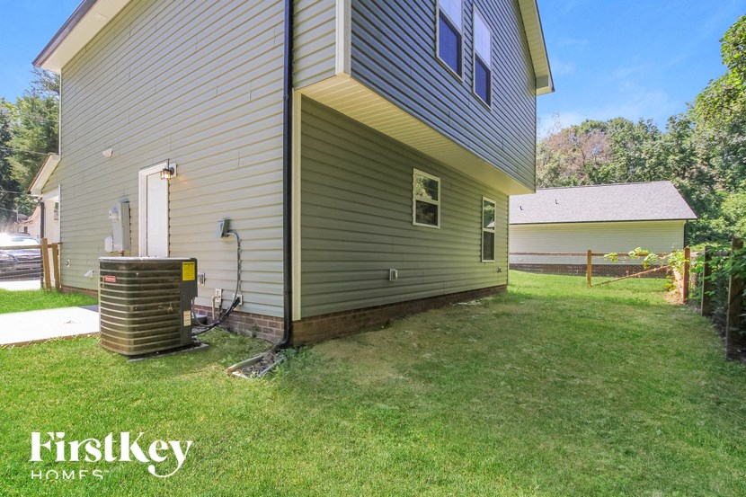 A house with a grey siding and a brown roof is shown with a grassy lawn in front.