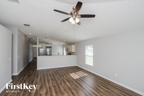 an empty living room with a ceiling fan and a kitchen