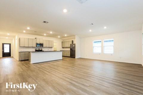 A spacious kitchen and living room with wooden floors and white walls.