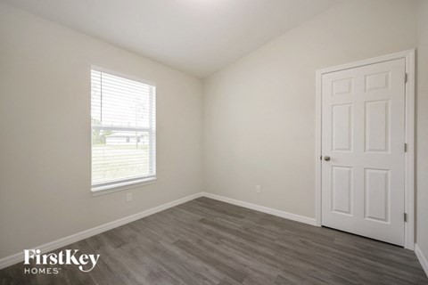 a bedroom with a white door and wood flooring and a window
