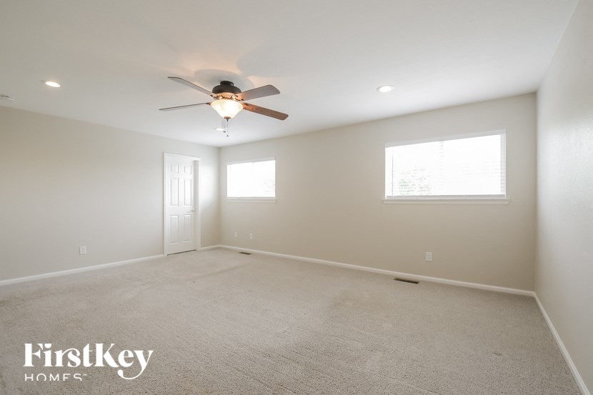 A spacious room with a ceiling fan and two windows.