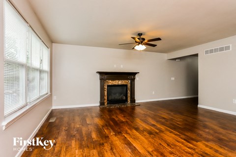 a living room with a fireplace and wooden floors and a ceiling fan