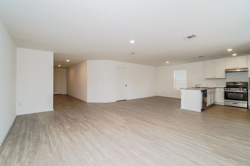 an empty living room and kitchen with white walls and wood flooring