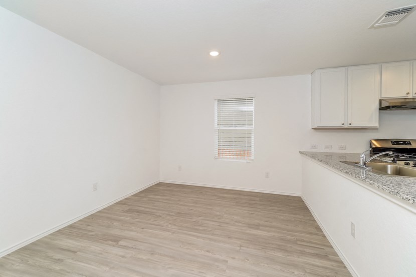 the living room and kitchen of an apartment with white walls and wood flooring