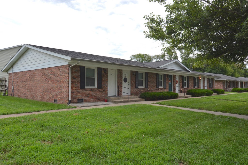 the front of a brick house with a porch and a lawn