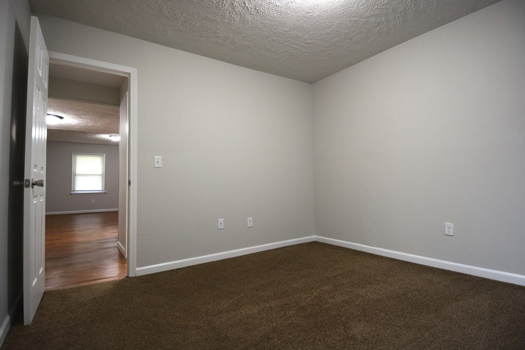 an empty living room with carpet and a door to a bedroom