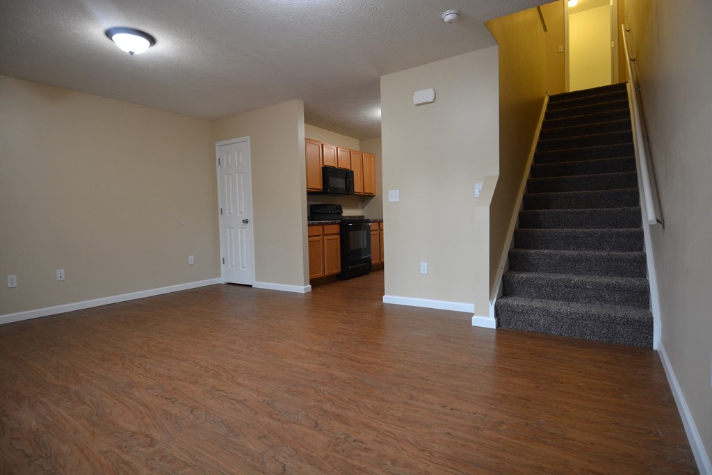 an empty living room with a staircase and a kitchen