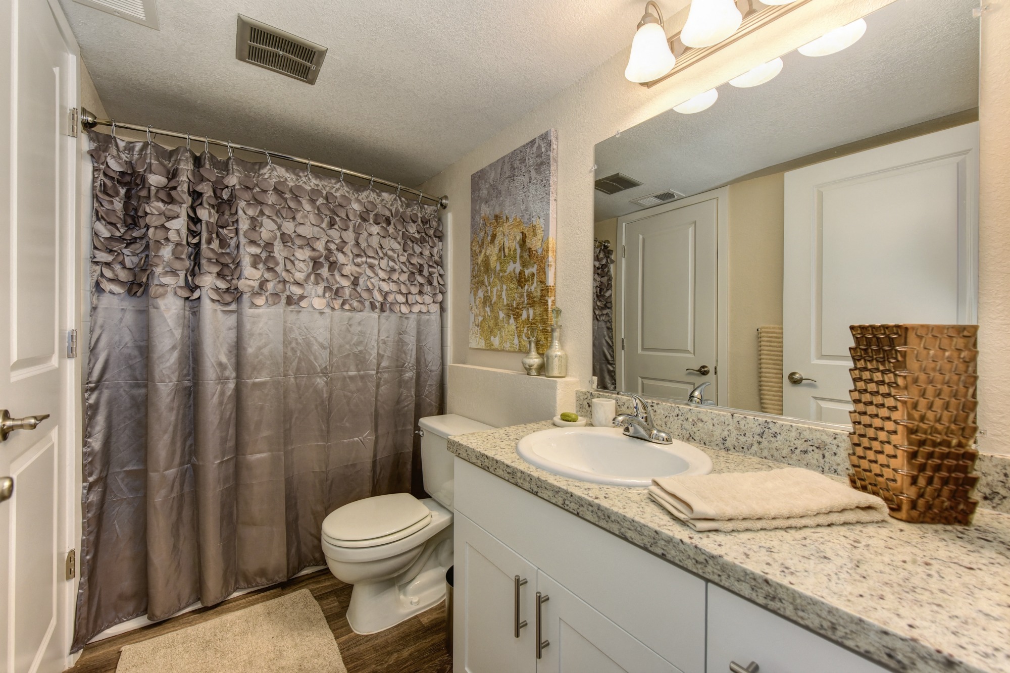 Bathroom with Granite Countertops, Toilet, Silver Shower Curtains, White Cabinets and Vanity at Rush River Apartments, California