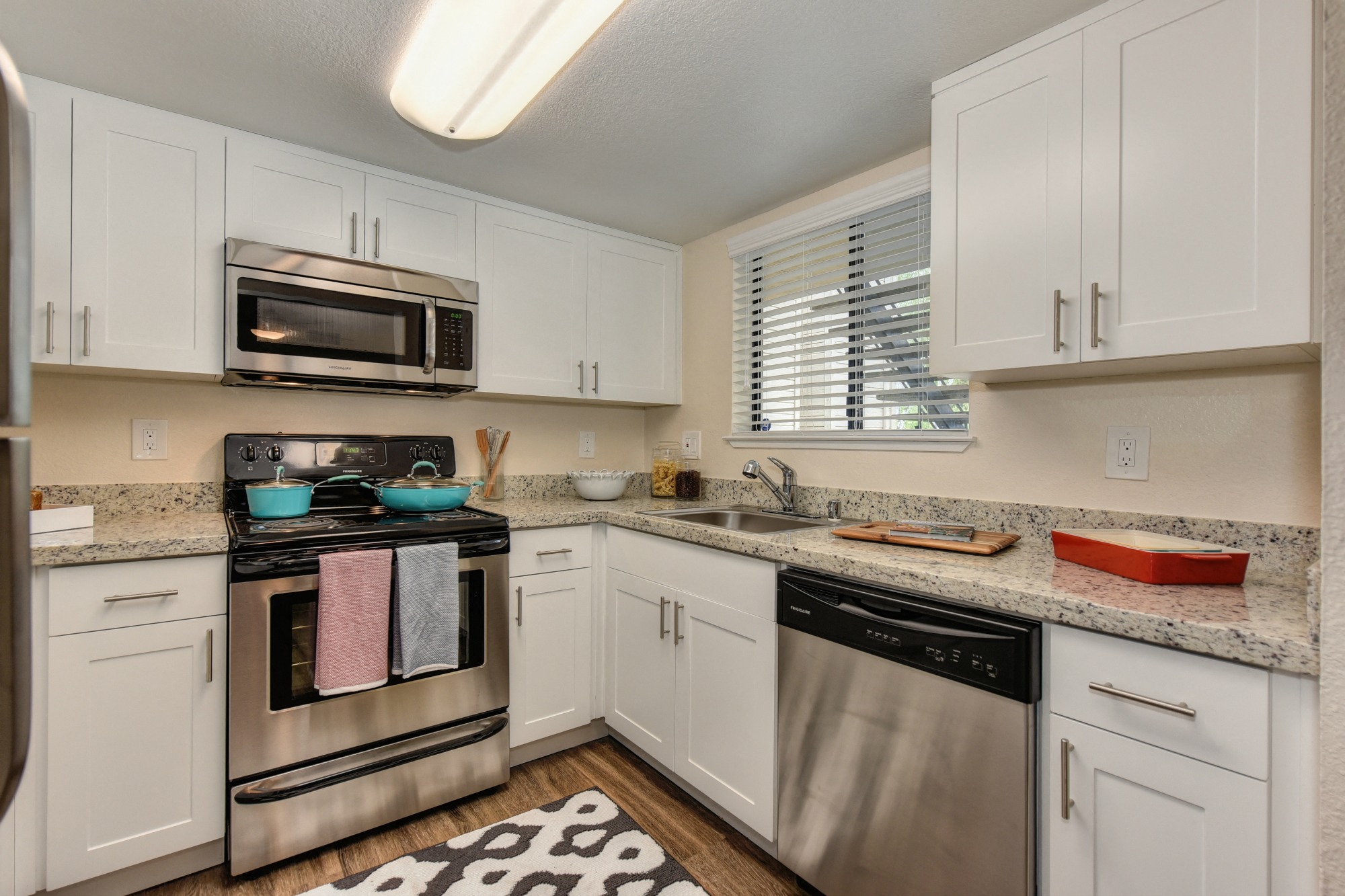 Kitchen with Granite Counters, Dishwasher, Oven, Microwave, Black/White Rug and White Cabinents at Rush River Apartments, Sacramento, CA, 95831