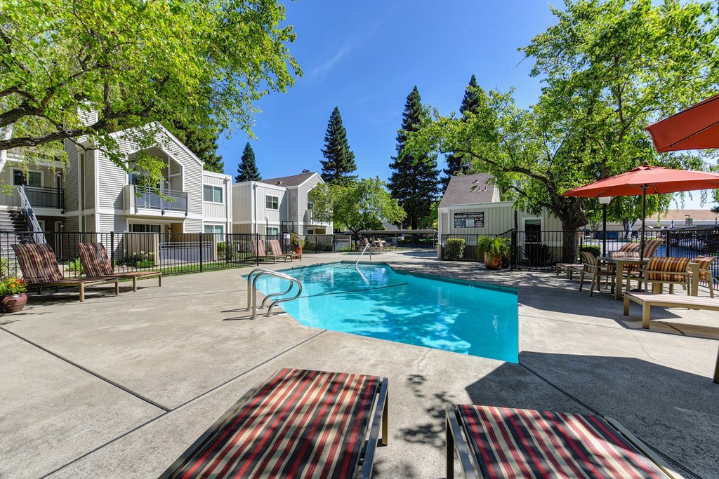 Pool Area with Trees, Red/White/Black Lines Runing Down Lounge Chairs and Apartment Exteriors at Rush River Apartments, Sacramento, 95831