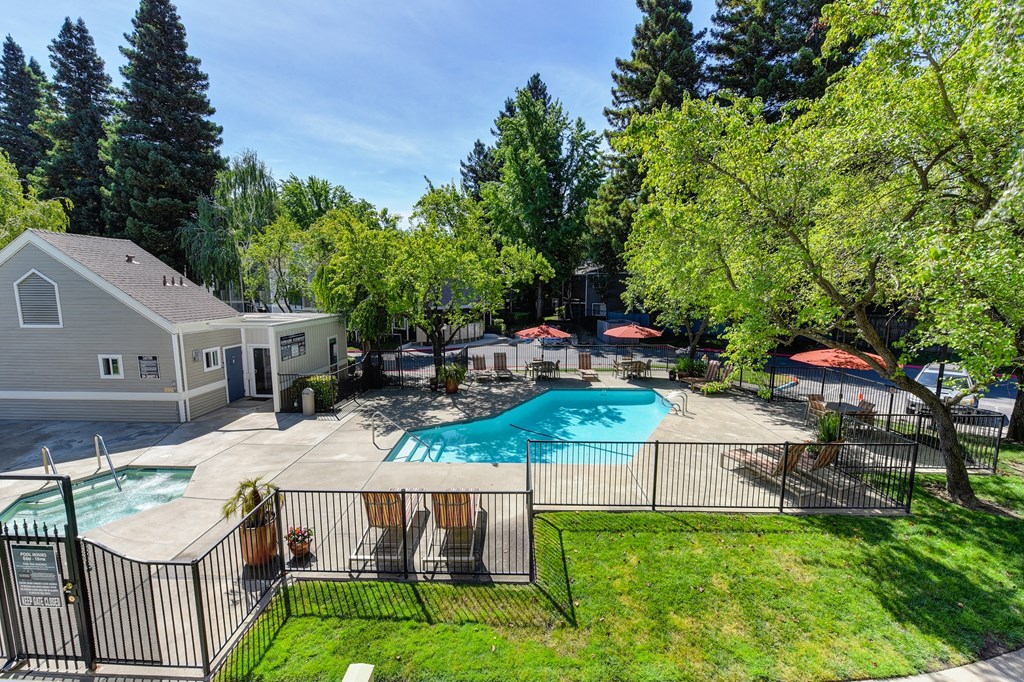Upper View of Pool Area with Grass, Gates and Orange Patio Umbrellas at Rush River Apartments, Sacramento