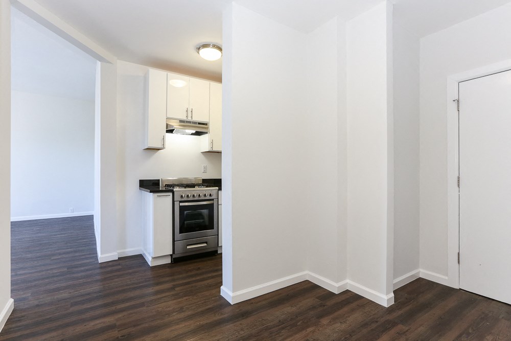 a living room and kitchen with white walls and wood flooring