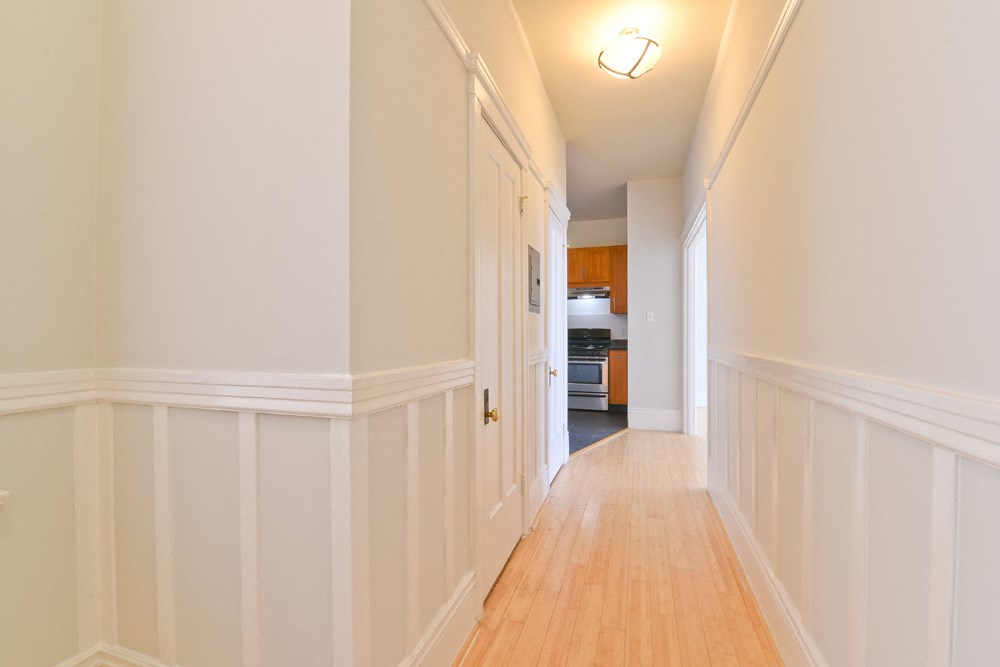 a long hallway with white walls and a door to a kitchen