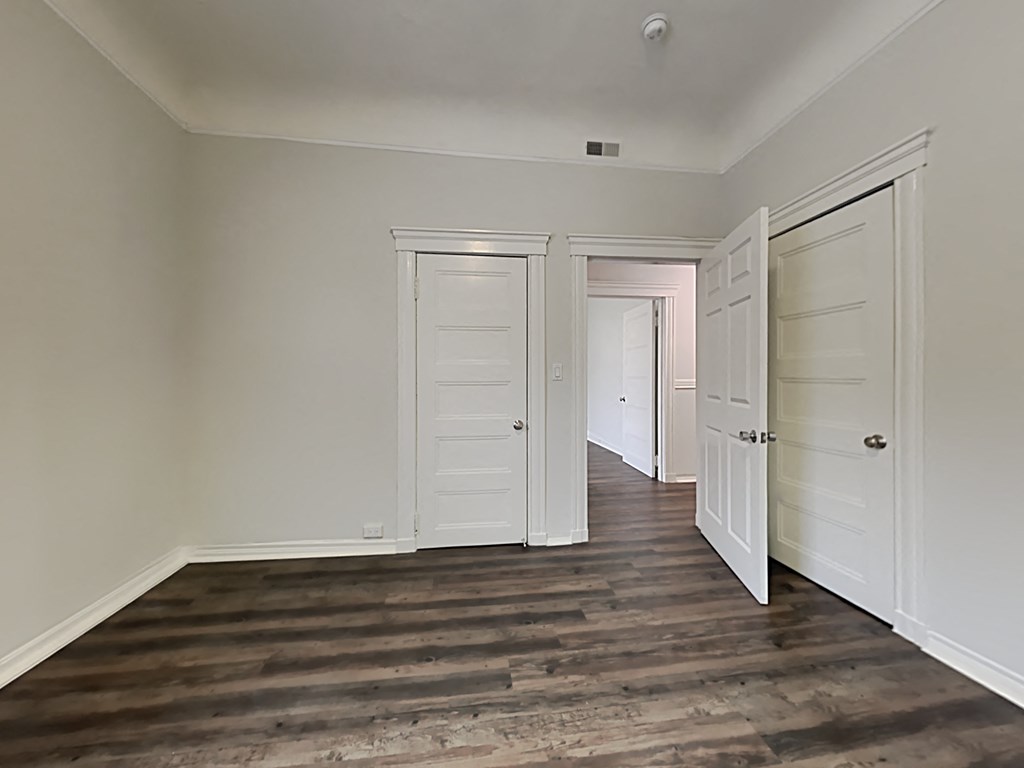 a bedroom with white doors and a hallway with wood flooring