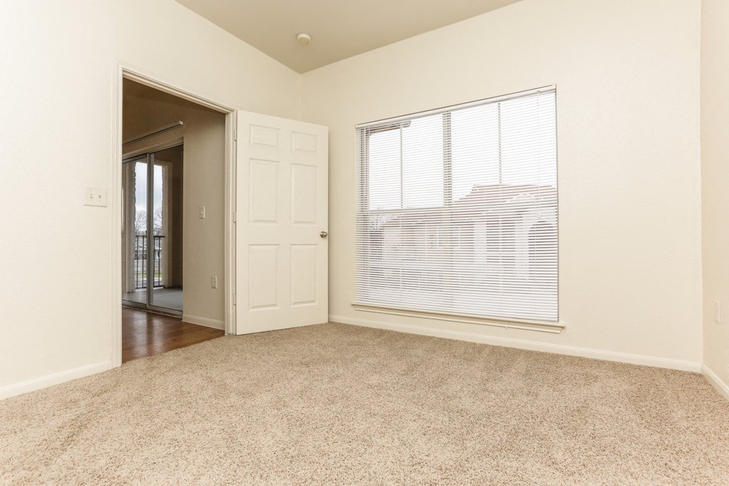 an empty living room with a large window and a door to a hallway