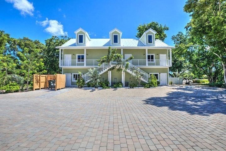 A large white house with a blue roof and a brick driveway.
