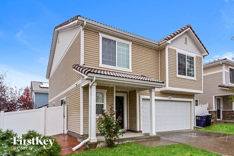 a tan house with a white fence and a driveway