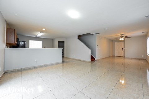 a large empty living room with a white tile floor and a ceiling fan
