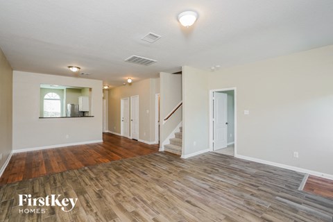 A spacious room with wooden flooring and a staircase leading to another room.