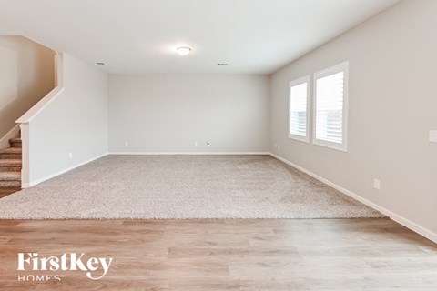 A spacious room with a staircase on the left and a rug on the floor.