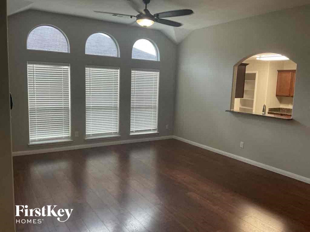 A room with a ceiling fan and a view of a kitchen through a window.
