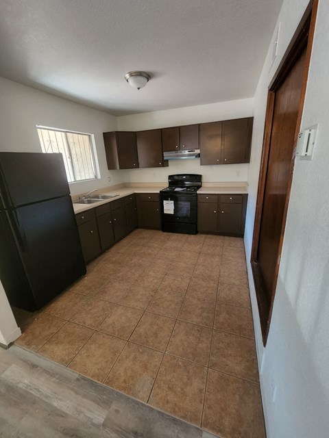 an empty kitchen with black appliances and brown tile flooring
