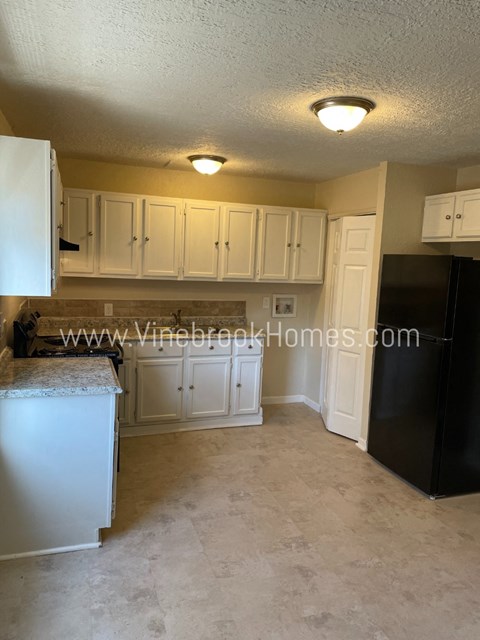 A kitchen with a black refrigerator and white cabinets.