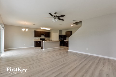 A spacious living room with a kitchenette in the background and a staircase leading to another level.