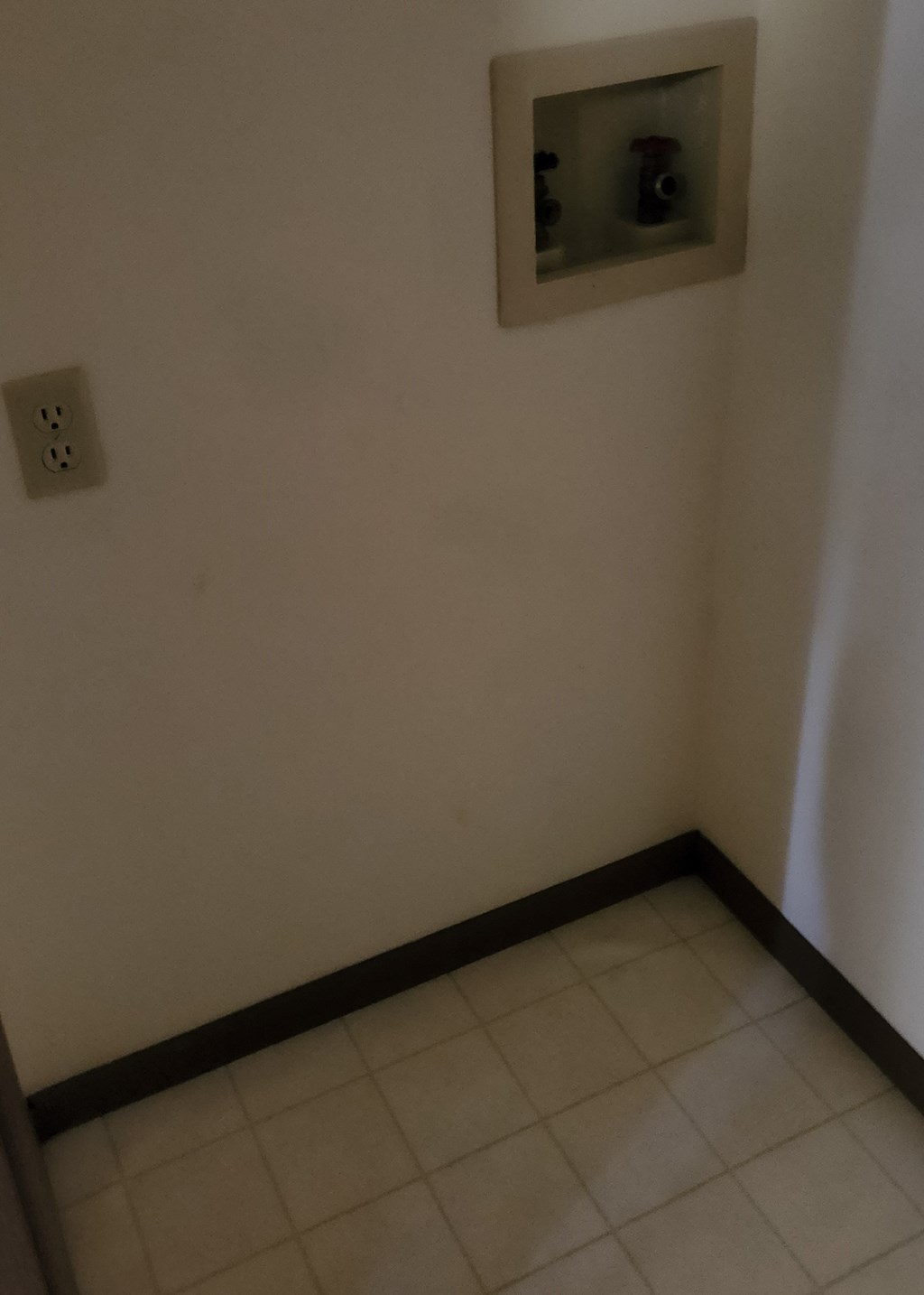 a small room with a tiled floor and a wall with an electrical outlet