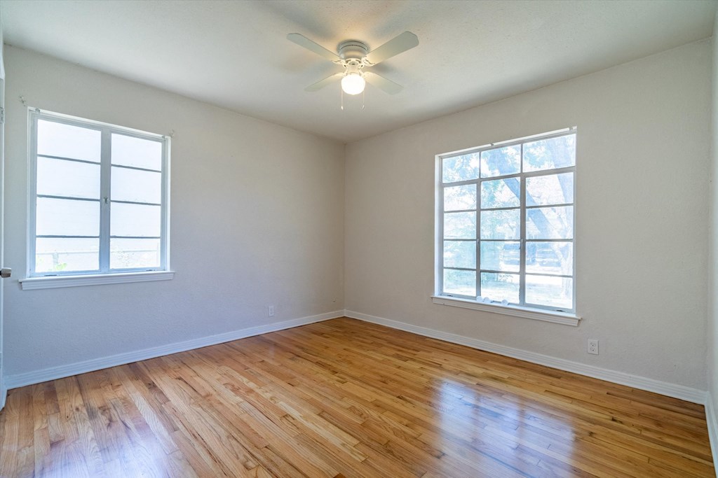 an empty living room with a ceiling fan and two windows