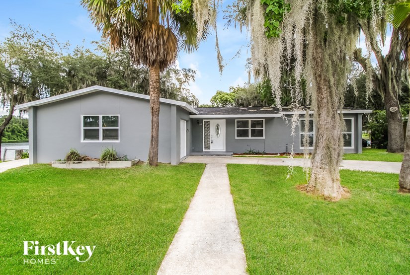 A grey house with a white door and windows is surrounded by green grass and trees.
