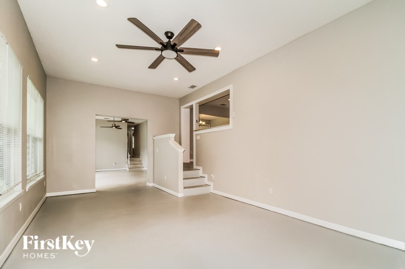 A spacious room with a ceiling fan and a staircase leading to another room.