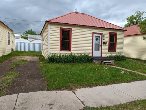 a small yellow house with a red roof and a sidewalk