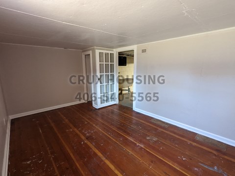 a small living room with a wooden floor and a door to a dining room
