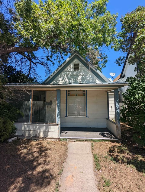 A small house with a porch and a tree in front.