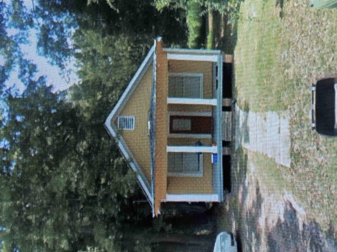 A small house with a brown roof and a white door is surrounded by trees.