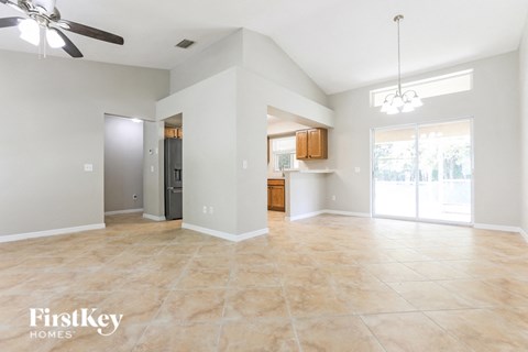 an empty living room with a kitchen and a ceiling fan