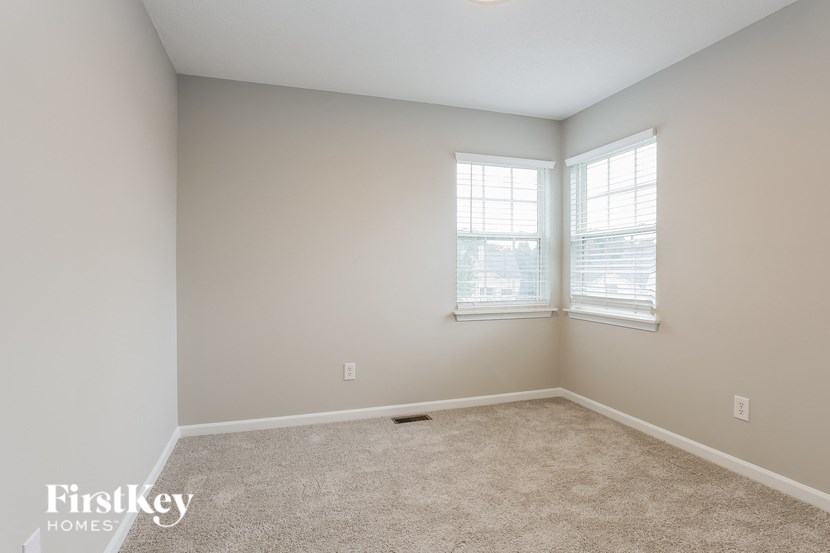 A room with a carpeted floor and two windows.