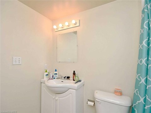 A bathroom with a white sink and toilet, a mirror with lights above it, and a blue shower curtain.