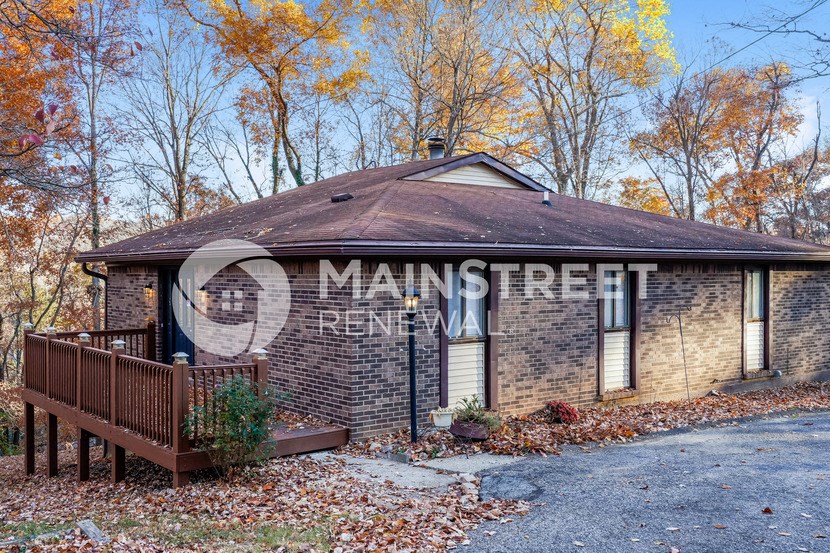 a small brick house with a deck and trees in the background