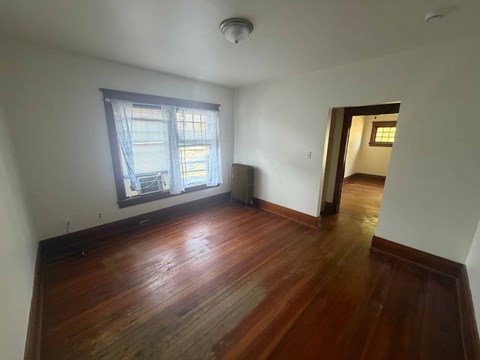 A room with wooden floors and a window with a view of a building outside.