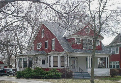 A red house with white trim and a black car parked in front.