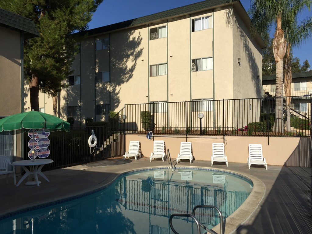 a swimming pool with chairs and an umbrella in front of a building