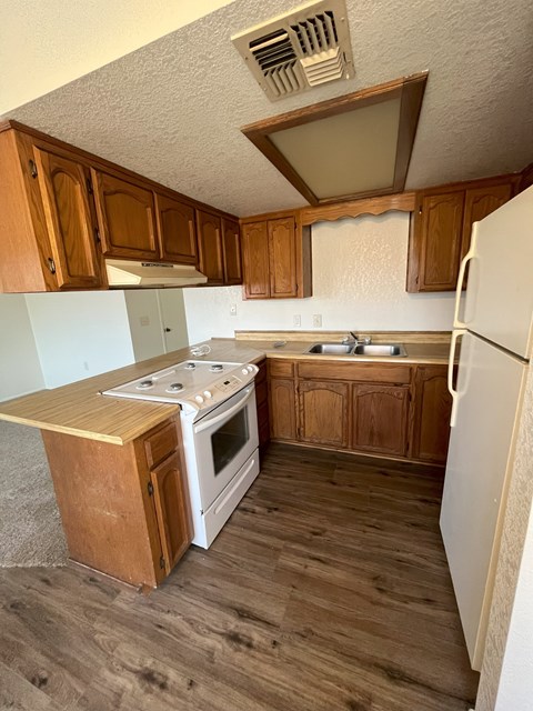 A kitchen with a white fridge, white stove and wooden cabinets.